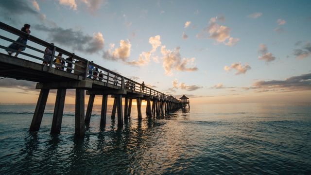 Sunset over an ocean pier with people enjoying the view and a calm atmosphere. Suitable for travel promotions, vacation planning, relaxation themes, and inspirational visuals.
