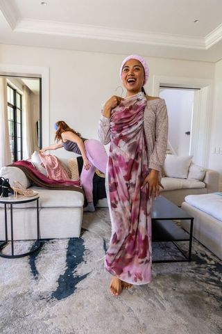 African american women styling long pink print dress while sorting fabrics in living room