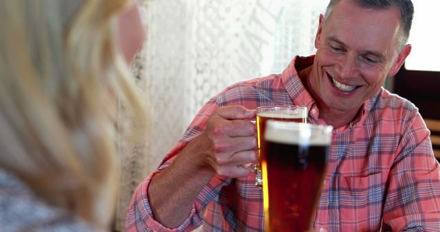 Mature friends enjoying a drink at a pub, clinking glasses, and smiling warmly. Great for use in advertising for breweries, pubs, social gatherings, and leisure activities. Can also be used in articles about social life, friendships, and enjoying free time.