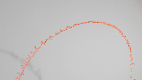 Orange Paint Arcing in Slow Motion Against Light Background