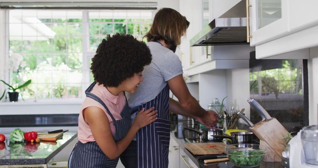 Couple sharing a fun cooking experience in a modern kitchen. Use to represent themes of domestic life, healthy living, and relationships in promotional material, culinary blogs, or advertisements.