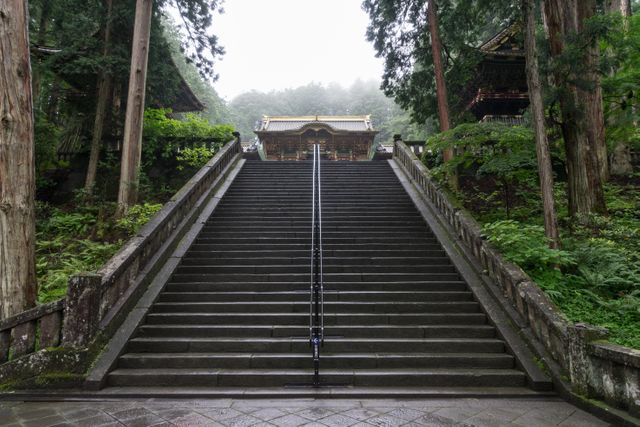 Majestic stone staircase leading to a traditional Japanese temple surrounded by lush greenery. The mist adds a mystical ambiance. Ideal for travel blogs, cultural heritage websites, and peaceful retreat promotions.