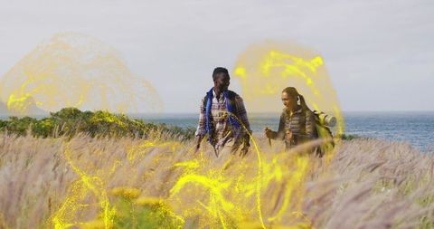 Coastal hiking couple walking through tall dune grass with golden light trail overlay