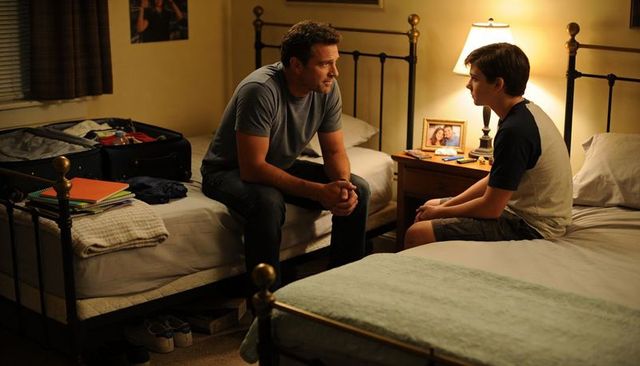 Father and teenage son having heartfelt conversation on twin beds by lamplight