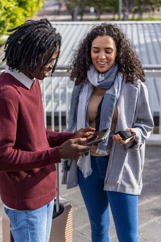 Friends sharing travel plans on phones beside rolling suitcase on urban rooftop terrace