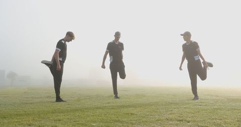 Athletic Teammates Stretching on Misty Morning Field
