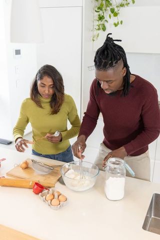 Indian woman and african american man baking together at island in bright modern kitchen