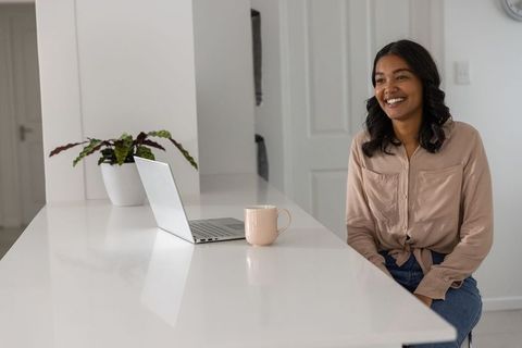 Modern home workspace woman smiling at kitchen island with laptop and pink mug