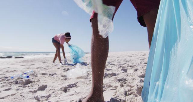 African american couple holding rubbish sacks and collecting rubbish from the beach. eco beach conservation.