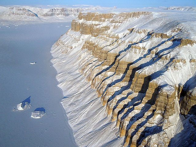 Showcasing the stunning snow-covered cliffs and frozen sea in Greenland, this image captures the striking natural beauty of Greenland's rugged terrain from an aerial perspective. The contrast of the white snow against the exposed stone and the widespread expanse of icy sea offers a glimpse into this remote and cold region of the world. Perfect for use in travel magazines, nature documentaries, geological studies, and environmental awareness campaigns, emphasizing the stark beauty and fragility of polar landscapes.