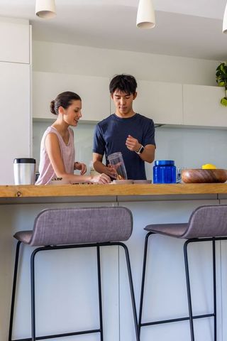 Young diverse couple preparing healthy smoothie at modern kitchen island home interior