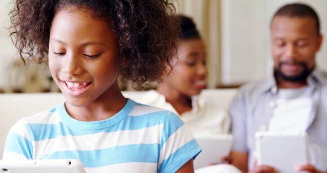 Smiling Girl Playing on Tablet with Family in Background - Download Free Stock Images Pikwizard.com