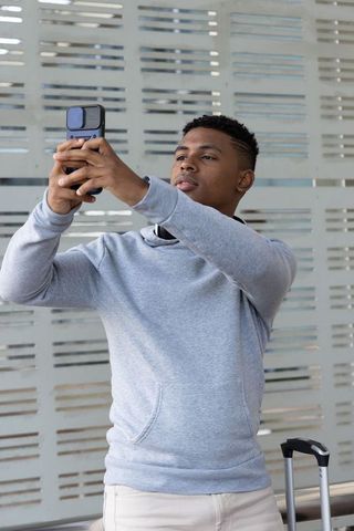 African american traveler taking selfie at modern transit concourse with carry-on luggage