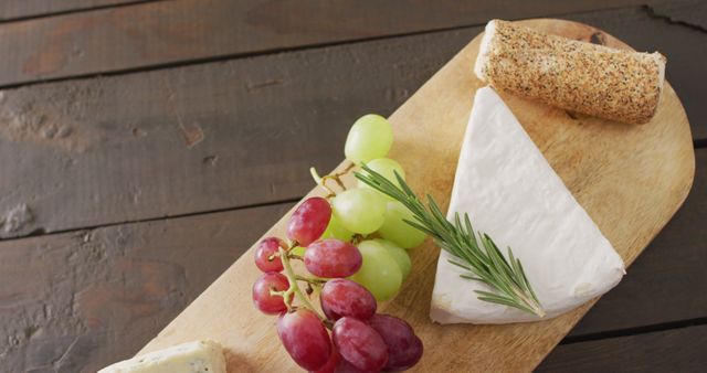 Image of cheeses, grapes, nuts and rosemary on chopping board, on wooden table with copy space. quality, tasty light food snack.