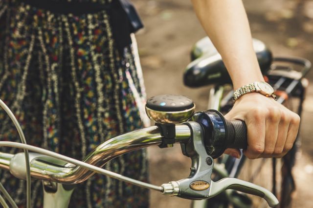 Image of a woman's hand holding a bicycle handlebar, showing details of the grip and her wristwatch. Ideal for use in designs promoting outdoor activities, women's cycling, healthy lifestyles, and sustainable transport. Suitable for blogs, advertisements, lifestyle articles, and social media content related to cycling and wellness.