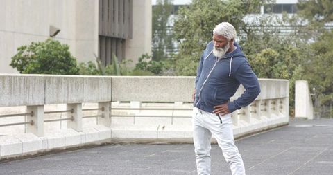 Senior african american man stretching hands-on-hips on urban concrete terrace in hoodie