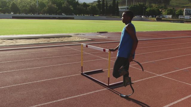 A determined athlete with prosthetic legs is seen preparing for a race on a sunny track. He is leaning on a hurdle and stretching, exemplifying strength and perseverance. Perfect for use in stories and campaigns promoting inclusivity in sports, motivation in athletics, or the capabilities of disabled athletes.