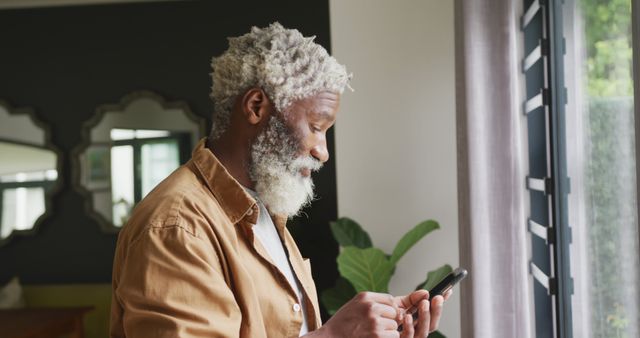 Senior Man Typing on Smartphone by the Window Smiling - Download Free Stock Images Pikwizard.com