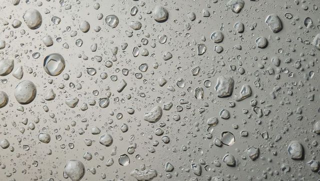 Water droplets beading on smooth gray surface with specular highlights and macro texture