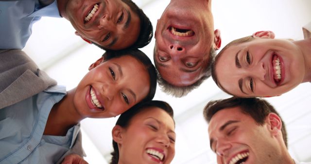 A diverse group of colleagues smiling and looking down at the camera. Their expressions suggest they are enjoying a light-hearted moment during a team bonding activity. This image can be used for promoting team-building programs, corporate culture, seminars, workshops, inclusive work environments, or advertisements that emphasize happiness and teamwork.