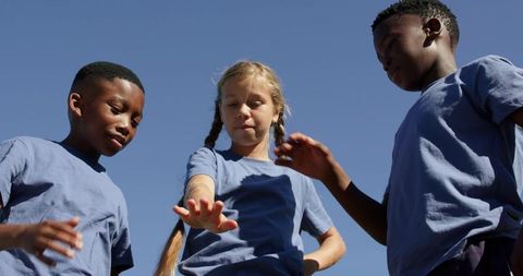 Multiracial children joining hands outdoors in matching blue shirts showing teamwork
