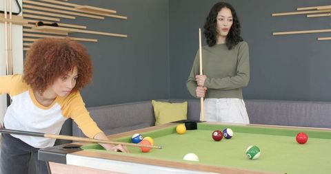 Diverse friends playing pool in modern lounge on green-felt table bonding over game