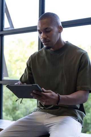 African american man using tablet by window natural light casual outfit remote work study