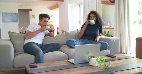 African American couple sipping coffee on sofa while watching laptop in cozy living room