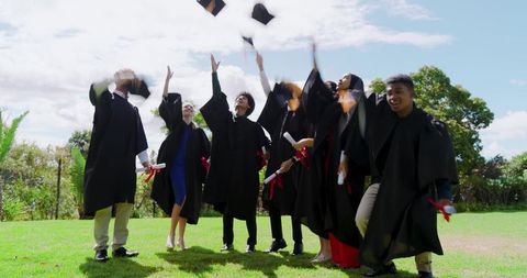 Diverse graduates throwing caps in air celebrating diplomas on campus lawn