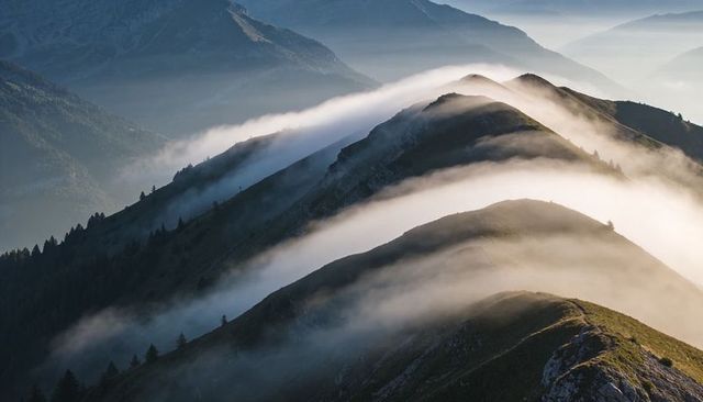 Fog flowing along sinuous alpine ridge at sunrise, mist rolling over grassy slopes