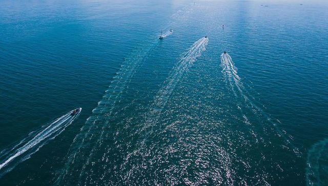 Aerial view of motorboats cutting turquoise ocean leaving white wake trails under sun