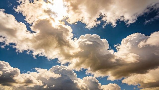 Golden backlit cumulus clouds towering across deep blue sky with sunlit rays