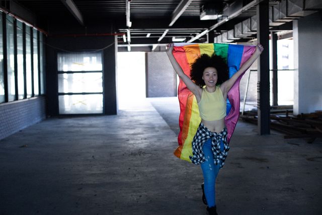 Transgender woman holding LGBT flag in an empty parking garage, celebrating diversity and gender expression. Ideal for use in campaigns promoting inclusivity, pride events, and gender identity awareness.