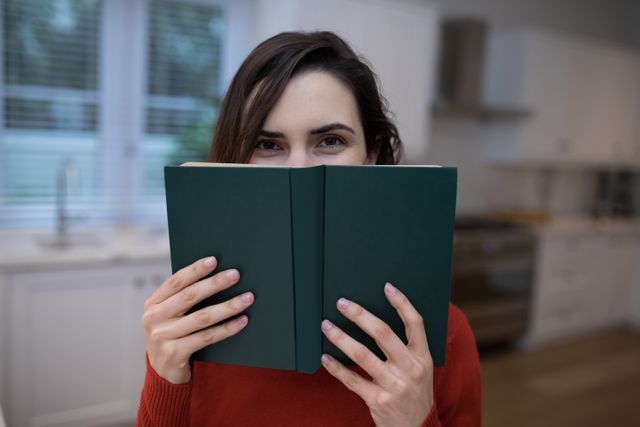 This image shows a woman holding a book in a modern kitchen, creating a cozy and relaxed atmosphere. Ideal for use in articles or advertisements related to reading, home life, relaxation, or modern living spaces.