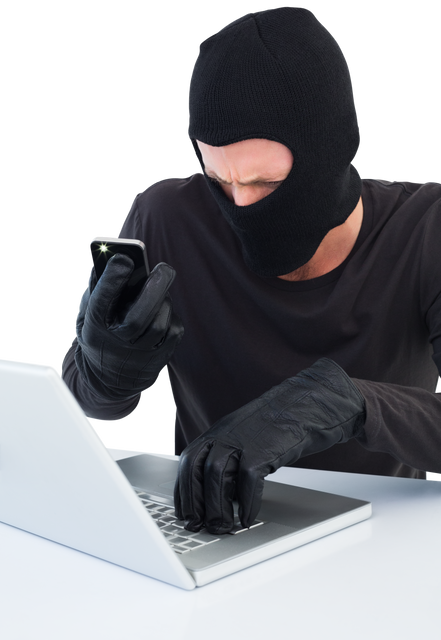 Depiction of a masked cybercriminal in dark clothing using a laptop and smartphone simultaneously. The person is wearing black gloves, expressing tension and concentration. Can be used in articles, presentations, or reports on internet security, high-tech crimes, identity theft, cybersecurity awareness campaigns, and materials warning against online fraud.