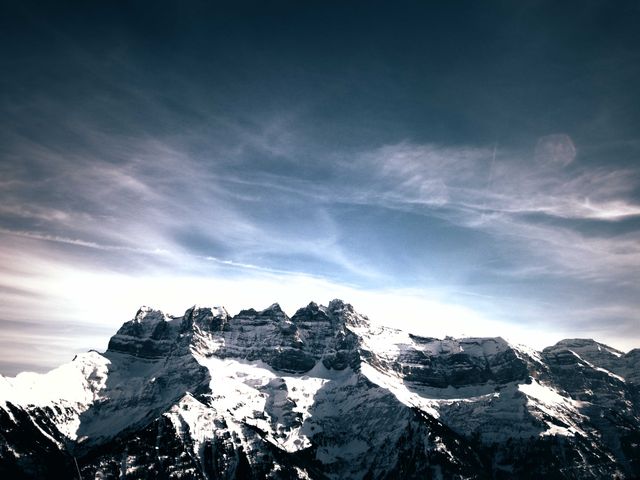 Stunning view of snow-capped mountain peaks under a cloudy sky. Ideal for nature, adventure, travel, and outdoor activities promotions. Suitable for posters, wallpapers, and websites featuring natural landscapes and winter themes.