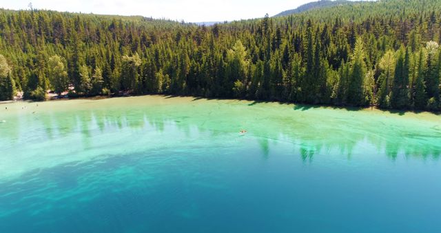 This drone view of a picturesque turquoise lake surrounded by dense forest provides a serene and tranquil scene. Ideal for promoting outdoor activities, travel destinations, nature conservation, and wellness retreats. Perfect for use in websites, brochures, or ads focusing on ecotourism and outdoor adventures.