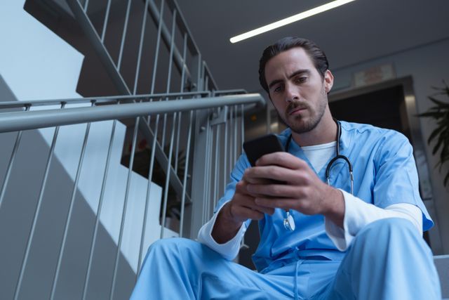 Low angle view of male surgeon using mobile phone while sitting on stairs at hospital