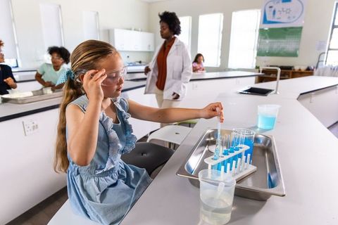 Elementary girl conducting chemistry experiment with pipette and test tubes in classroom