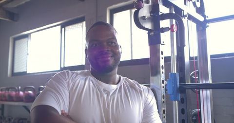 Smiling african american man standing arms crossed beside power rack in gym