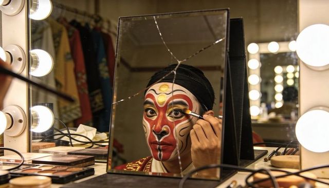 Actor applying traditional theatrical face paint backstage at vanity with cracked mirror