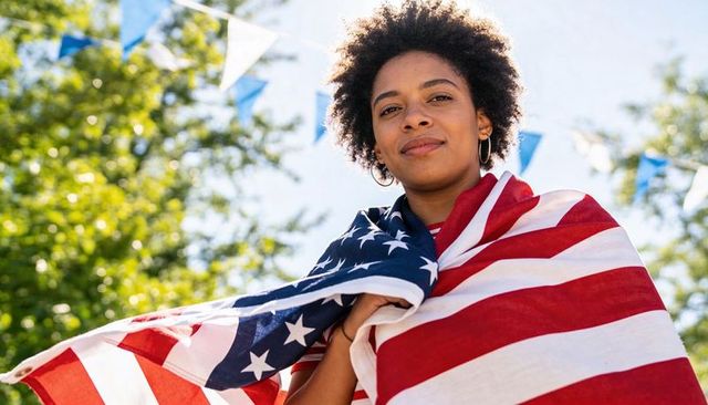 Confident young woman wrapping american flag while celebrating outdoors at summer festival