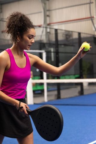 African american woman serving on indoor padel court in pink top and black skirt