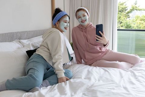 Relaxing spa night: diverse friends taking selfie on bed with face masks and loungewear