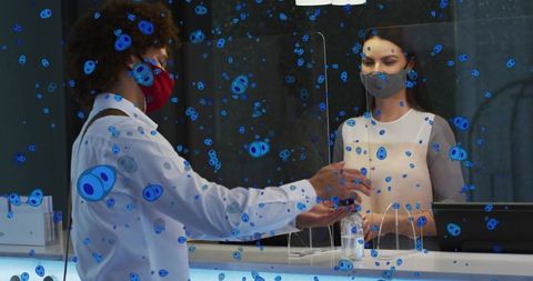 Passing card across plexiglass divider with masked customer and receptionist using sanitizer