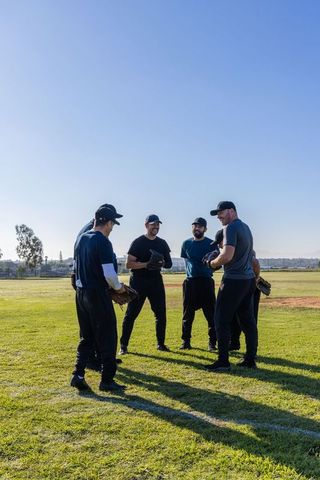 Baseball team huddle planning drills on sunlit suburban field showing leadership