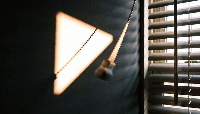 Sunlit blind pull casting triangle shadow on textured dark wall with slatted blinds