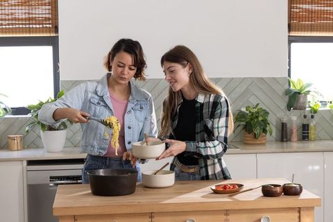 Friends serving fresh pasta on kitchen island during casual home cooking and meal prep