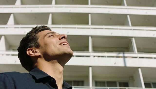 Urban man looking upward at modern white balcony facade with sunlit shadows and railings