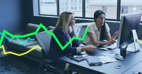 Businesswomen collaborating on data analysis in modern office with neon analytics graph